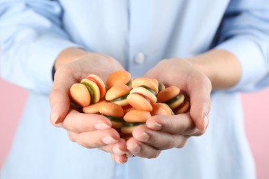 Woman holding handful of delicious gummy burger shaped candies on pink background, closeup