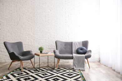Photo of Stylish sofa and armchair near brick wall in modern living room interior. Space for text