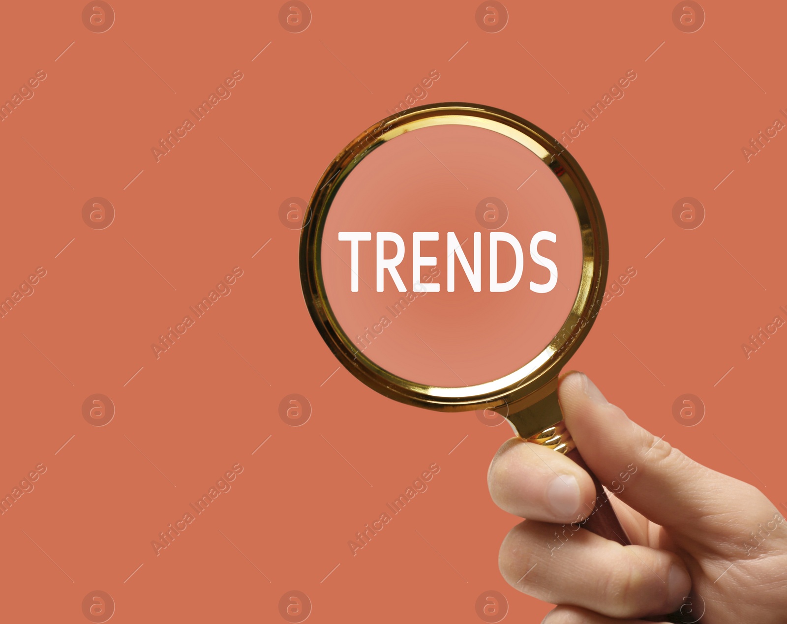 Image of Searching new and popular trends. Woman holding magnifying glass over word on coral background, closeup