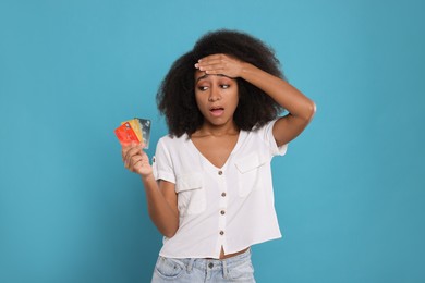 Shocked woman with credit cards on light blue background. Debt problem