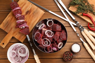 Photo of Flat lay composition with metal skewers and bowl of raw meat on wooden table