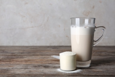 Photo of Glass cup with protein shake and scoop of powder on wooden table. Space for text