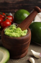 Mortar with delicious guacamole and ingredients on wooden table