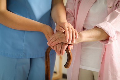 Elderly woman with walking cane and female caregiver indoors, closeup