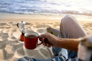 Photo of Man with cup of hot drink on sandy coast, closeup. Beach camping
