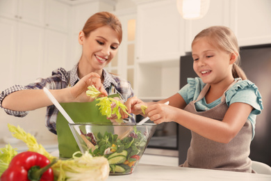 Photo of Mother and daughter cooking salad together in kitchen