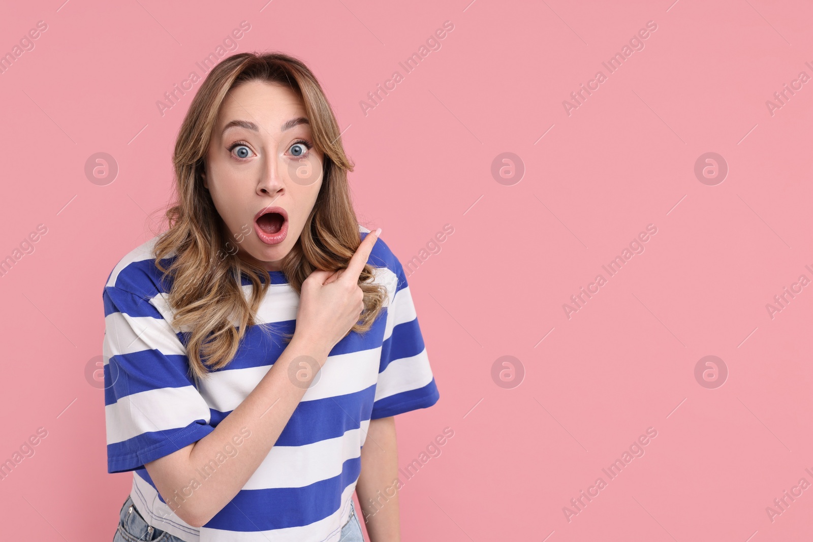 Photo of Portrait of surprised woman pointing at something on pink background. Space for text