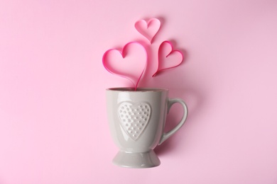 Cup and hearts made of ribbons on color background, top view