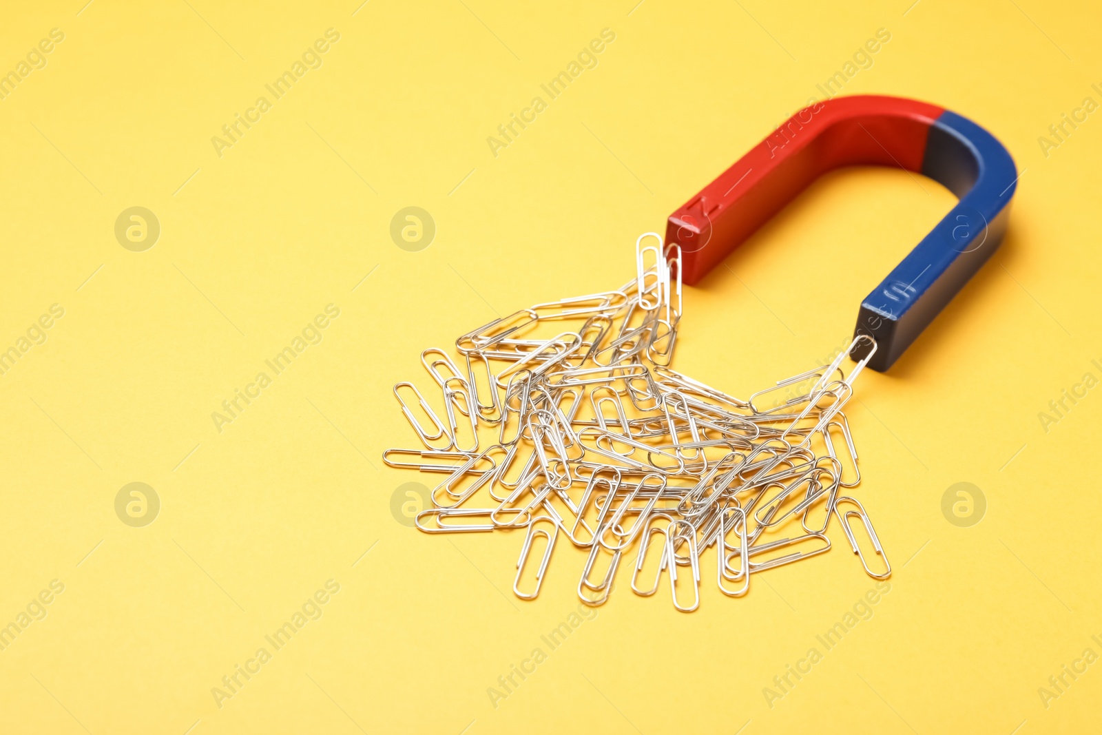 Photo of Magnet attracting paper clips on color background, space for text