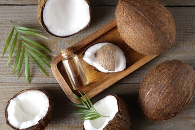 Photo of Bottle of organic coconut cooking oil, fresh fruits and leaves on wooden table, flat lay