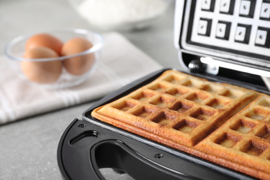 Photo of Modern iron with tasty Belgian waffles on grey table, closeup