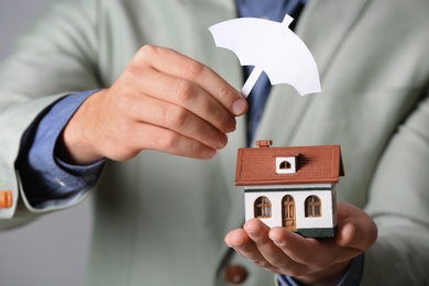 Male agent covering house model with umbrella cutout, closeup. Home insurance