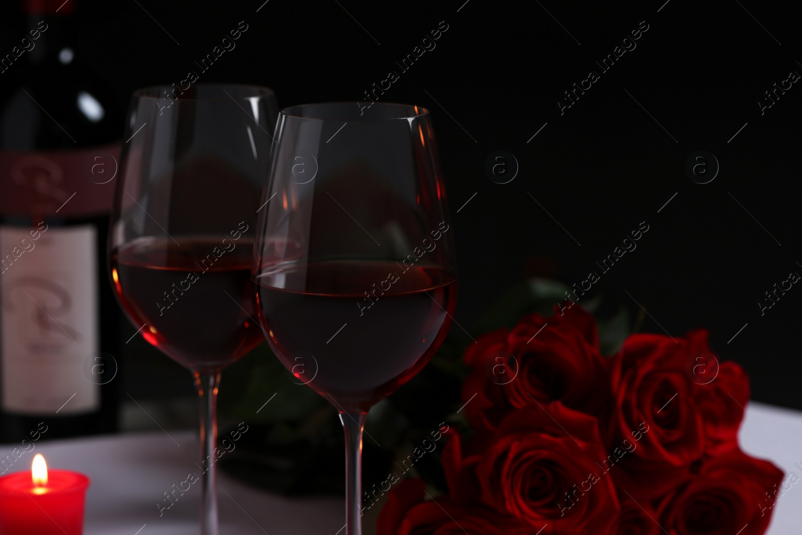 Photo of Glasses of red wine, rose flowers and burning candle on table, space for text. Romantic atmosphere