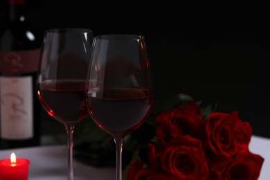 Glasses of red wine, rose flowers and burning candle on table, space for text. Romantic atmosphere