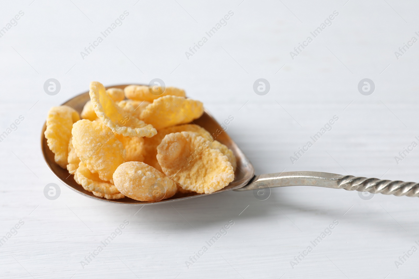 Photo of Metal spoon of tasty crispy corn flakes on white wooden table, closeup