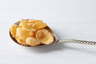 Photo of Metal spoon of tasty crispy corn flakes on white wooden table, closeup