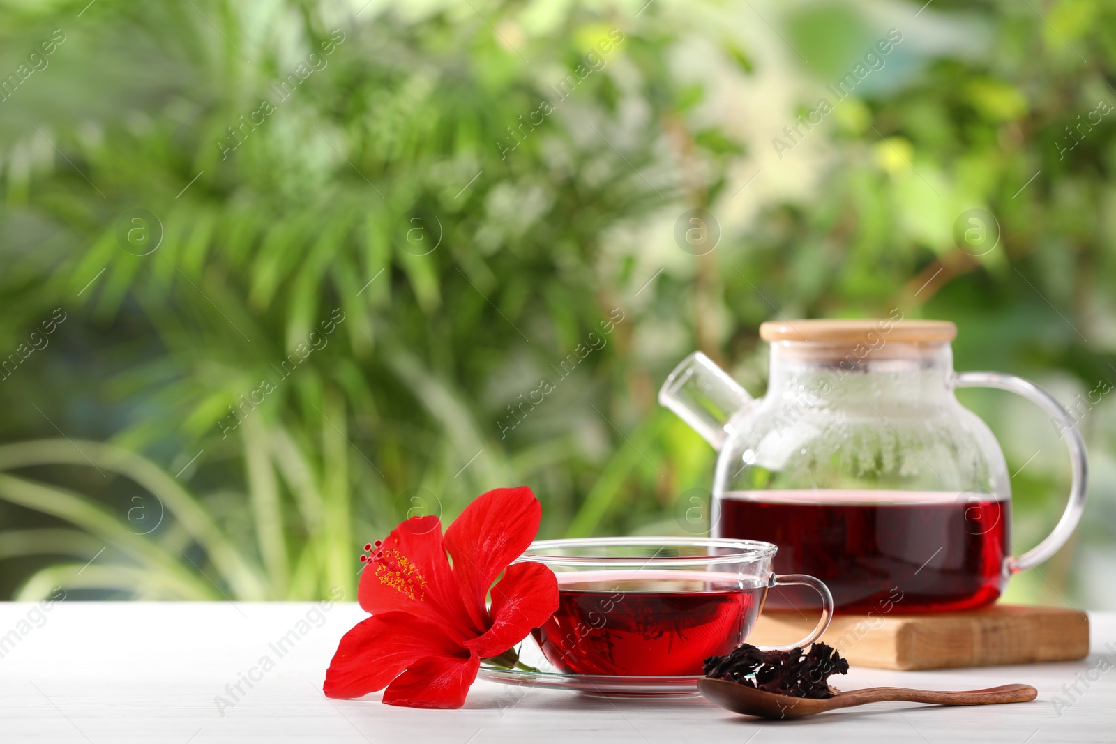 Photo of Delicious hibiscus tea and flowers on white wooden table outdoors, space for text