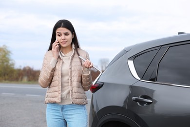 Photo of Worried young woman calling car service. Tire puncture