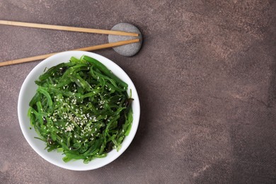 Photo of Tasty seaweed salad in bowl served on brown table, top view. Space for text