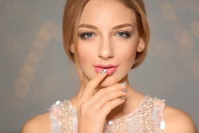 Beautiful young woman with shiny manicure on blurred background, closeup. Nail polish trends