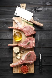 Photo of Fresh tomahawk beef cuts, spices and butcher tools on black wooden table, top view