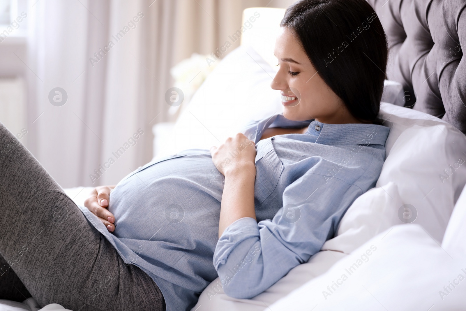 Photo of Young pregnant woman lying on bed at home