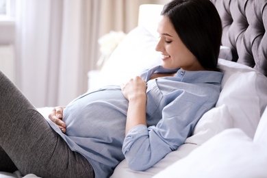 Photo of Young pregnant woman lying on bed at home