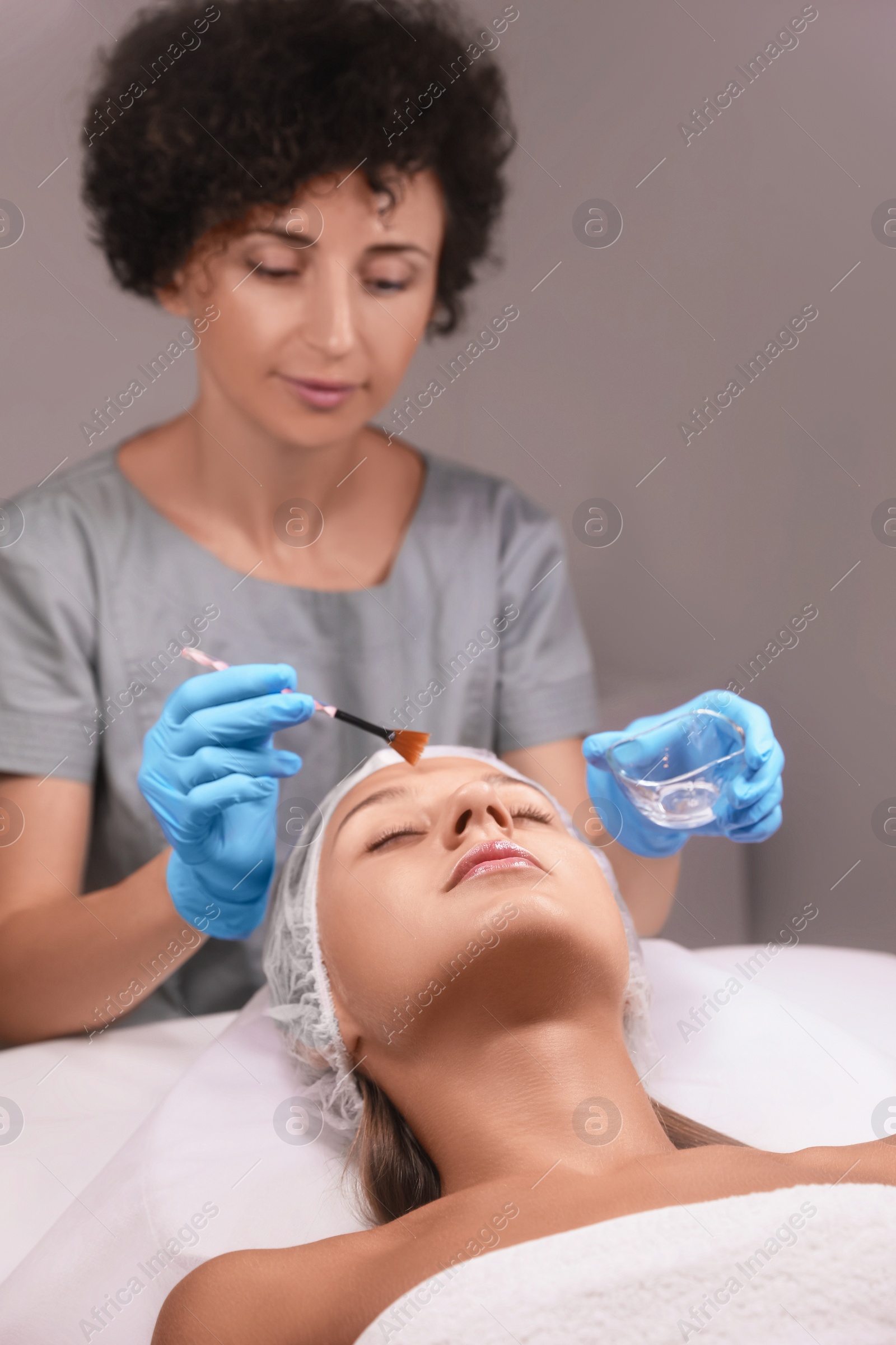 Photo of Cosmetologist applying cosmetic product for chemical peeling on client's face in salon