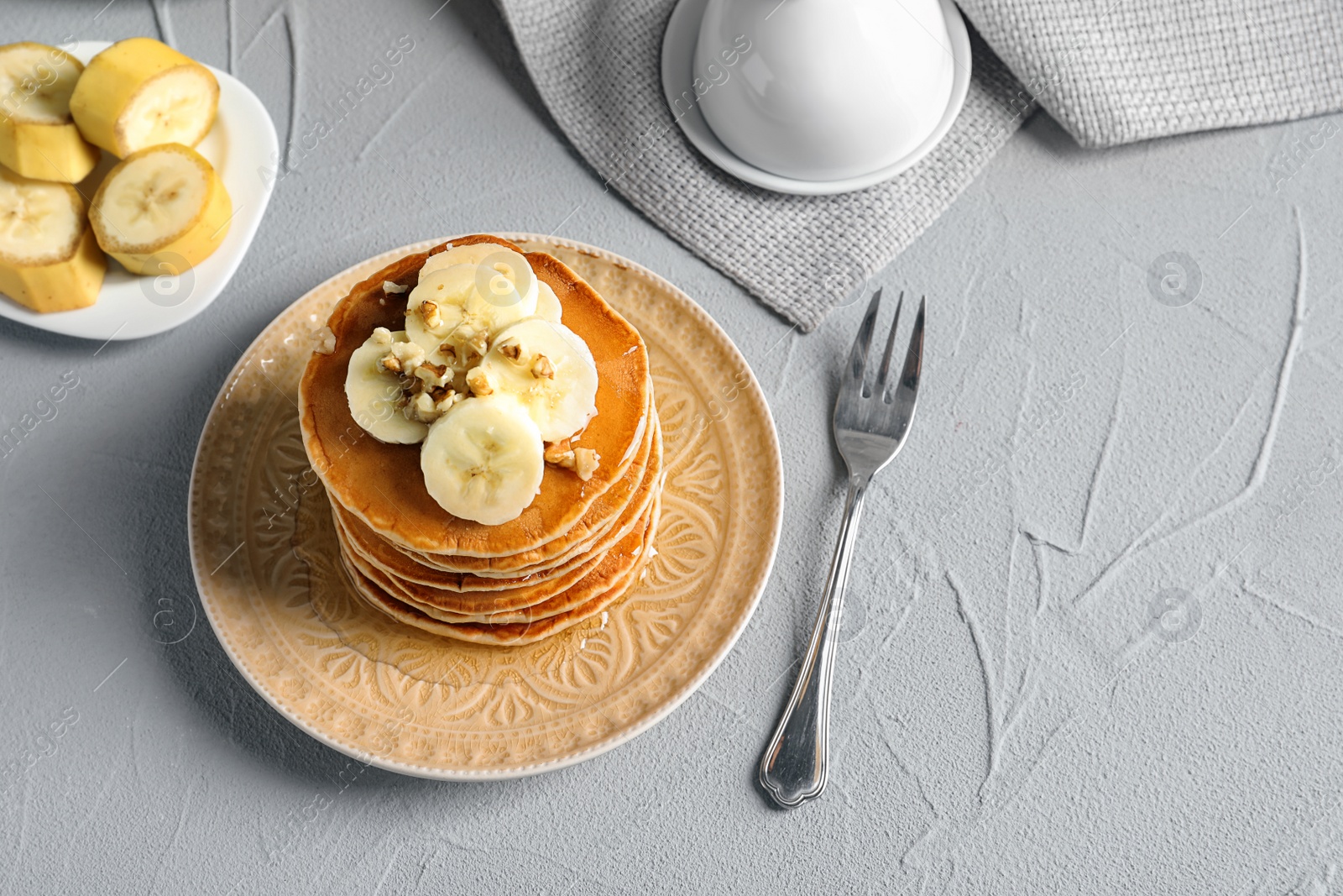 Photo of Stack of tasty pancakes with banana, nuts and honey on table