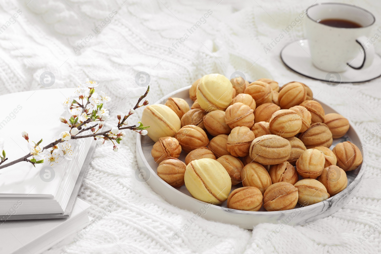 Photo of Delicious walnut shaped cookies with filling, cherry branch, notebook and cup of coffee on white knitted blanket. Homemade popular biscuits from childhood