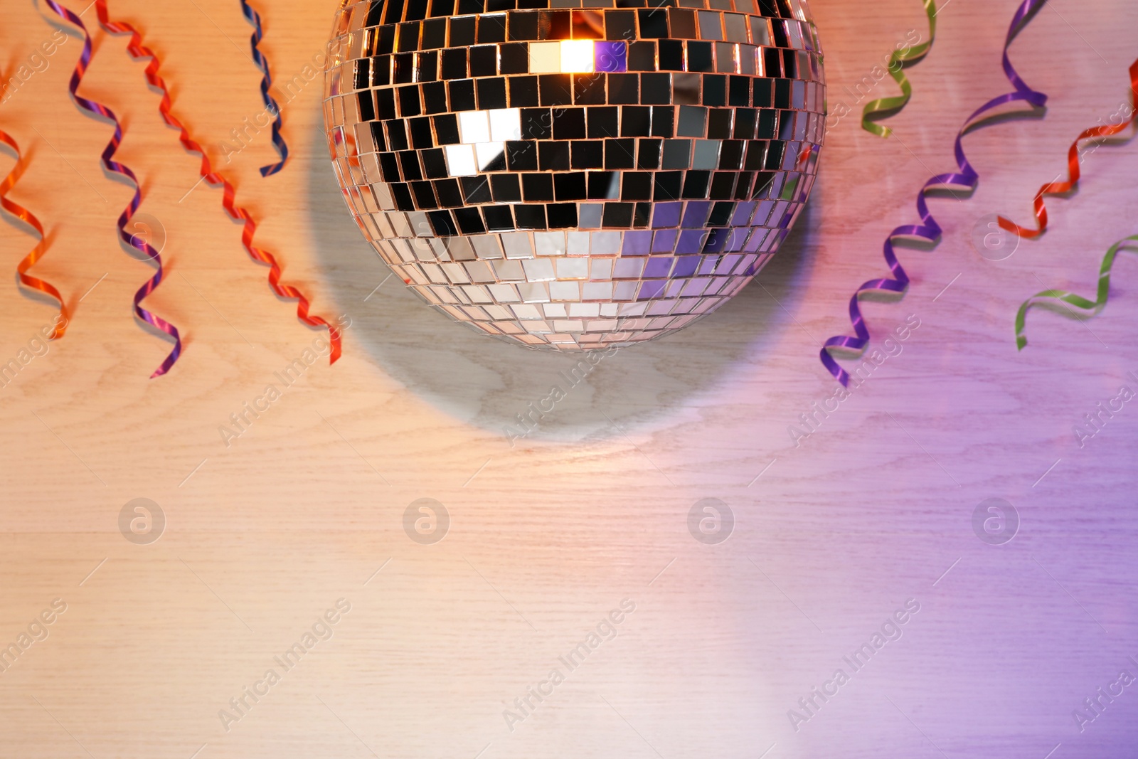 Photo of Shiny disco ball and serpentine streamers on white wooden background, flat lay. Space for text