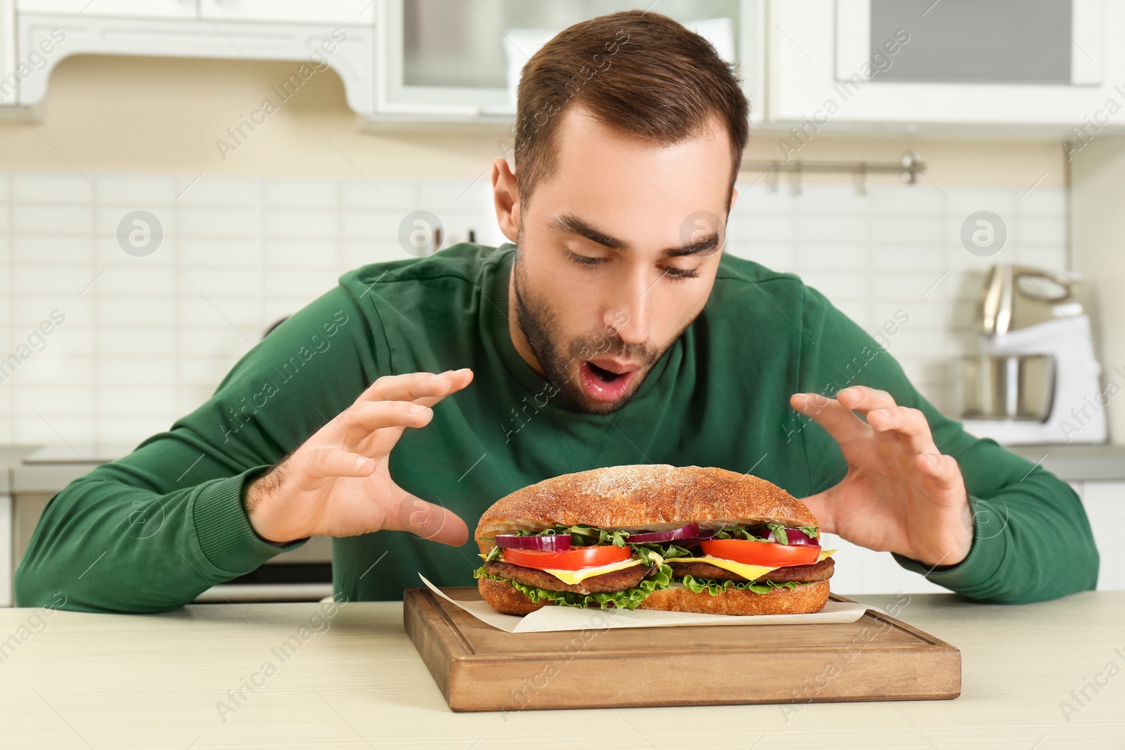 Photo of Young hungry man and tasty sandwich in kitchen