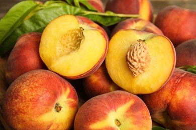 Pile of tasty peaches with leaves on plate, closeup