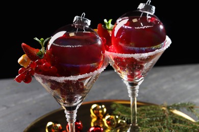 Photo of Creative presentation of Christmas Sangria cocktail in baubles and glasses on grey table against black background, closeup