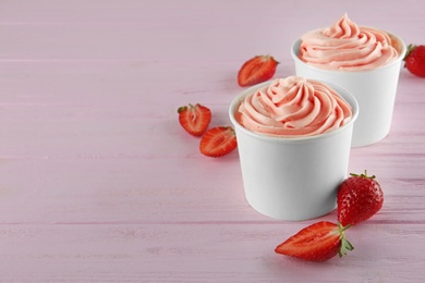 Cups with tasty frozen yogurt and strawberries on pink wooden table. Space for text