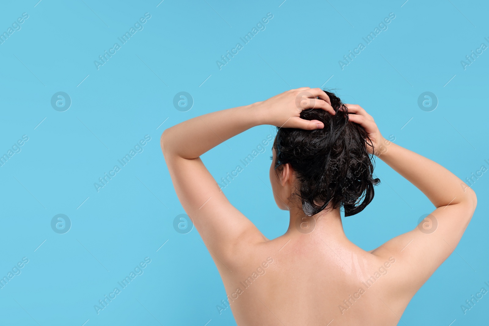 Photo of Woman washing hair on light blue background, back view. Space for text