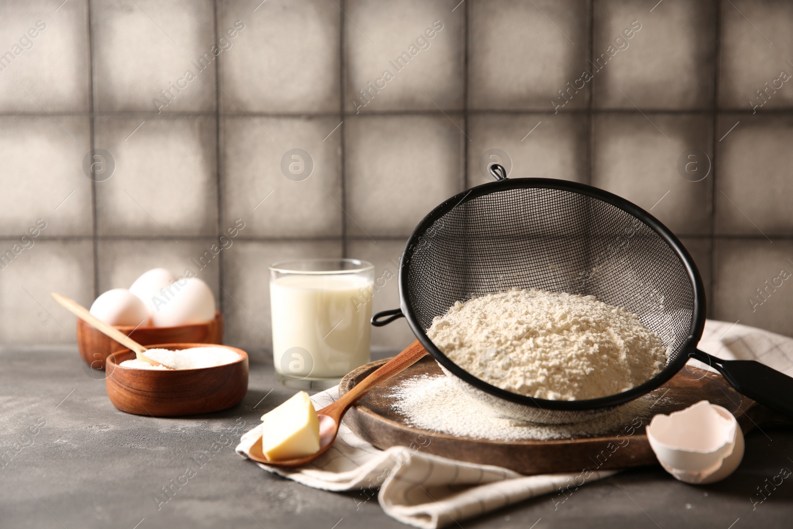 Photo of Making dough. Flour in sieve, spoon and butter on grey table, closeup