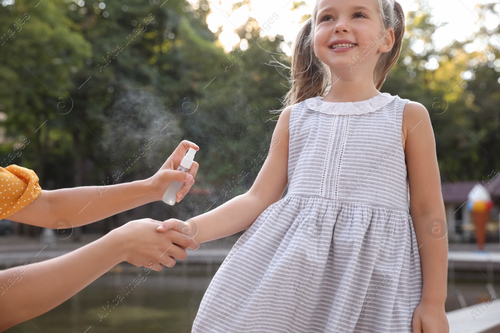Photo of Mother applying insect repellent onto girl's hand outdoors, closeup