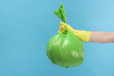 Photo of Woman holding plastic bag full of garbage on light blue background, closeup. Space for text