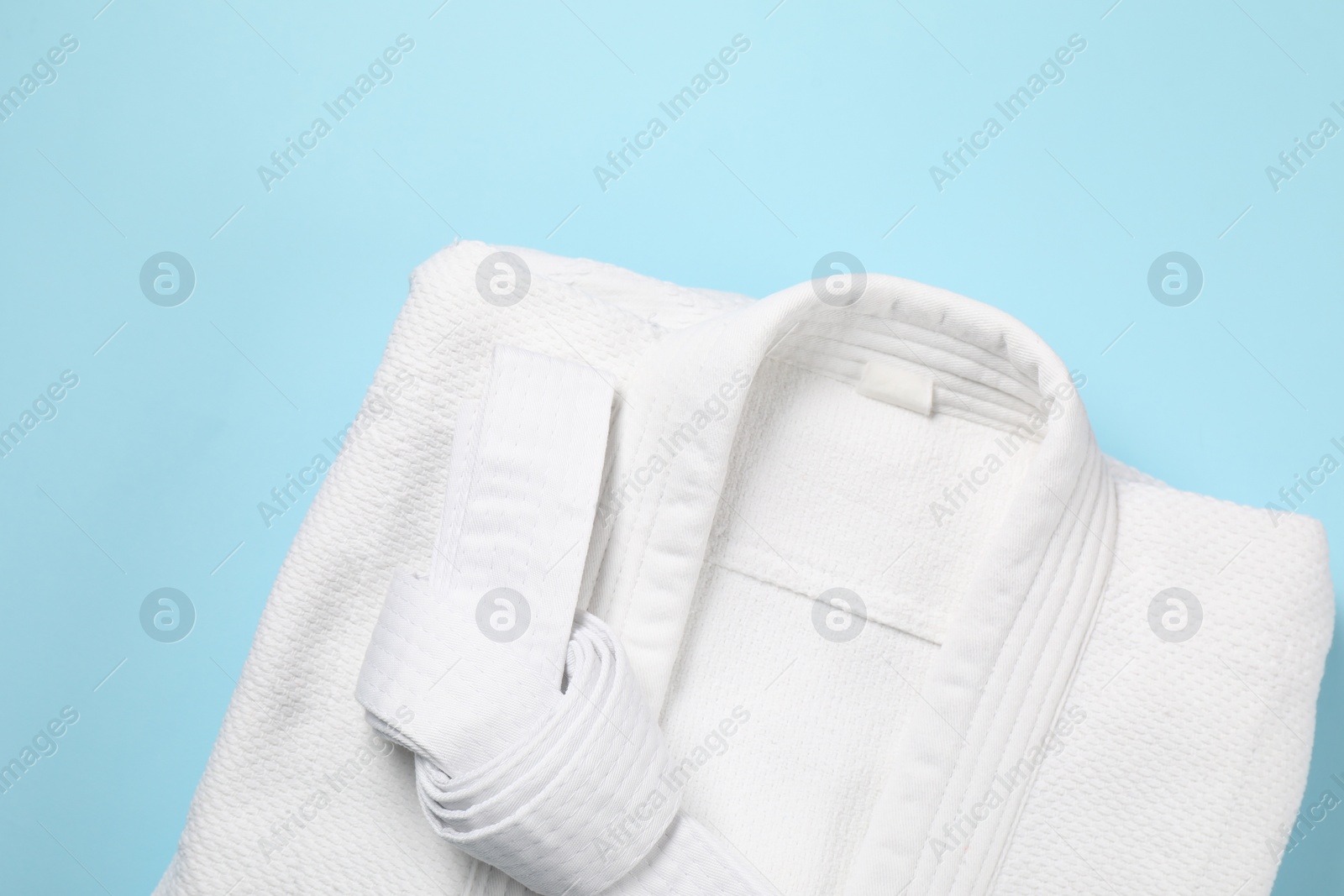 Photo of White karate belt and kimono on light blue background, top view