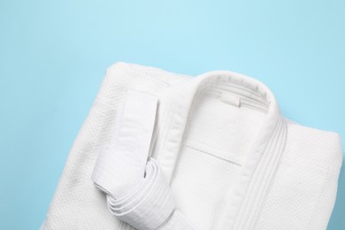 Photo of White karate belt and kimono on light blue background, top view