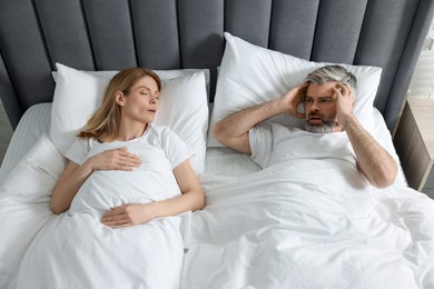 Photo of Irritated man lying near his snoring wife in bed at home