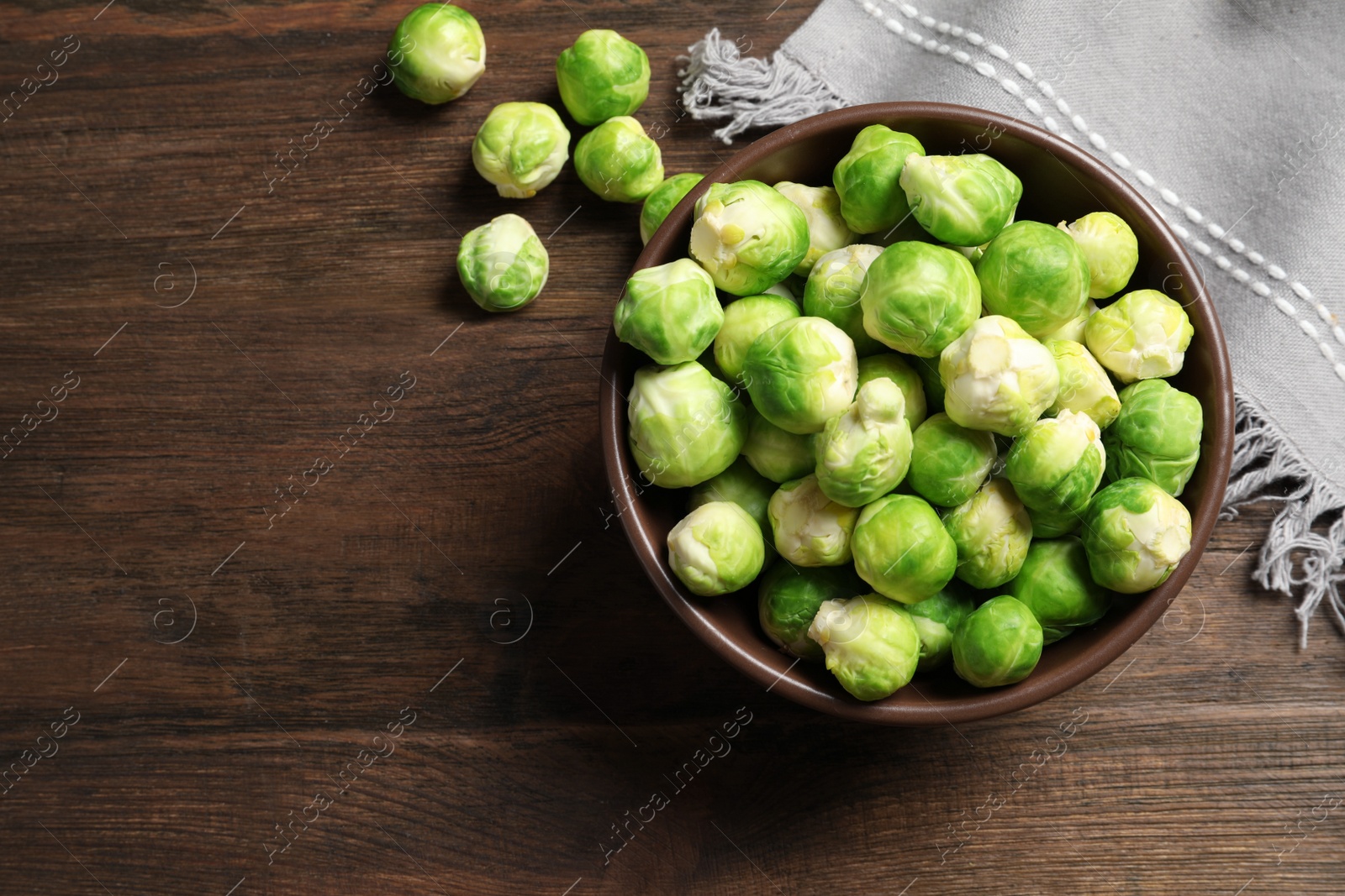 Photo of Bowl of fresh Brussels sprouts and napkin on wooden background, top view with space for text