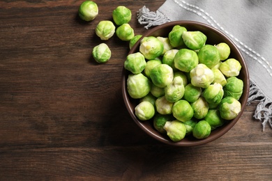 Photo of Bowl of fresh Brussels sprouts and napkin on wooden background, top view with space for text