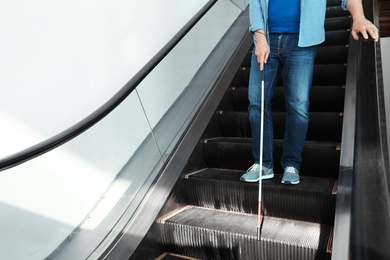 Blind person with long cane on escalator indoors. Space for text