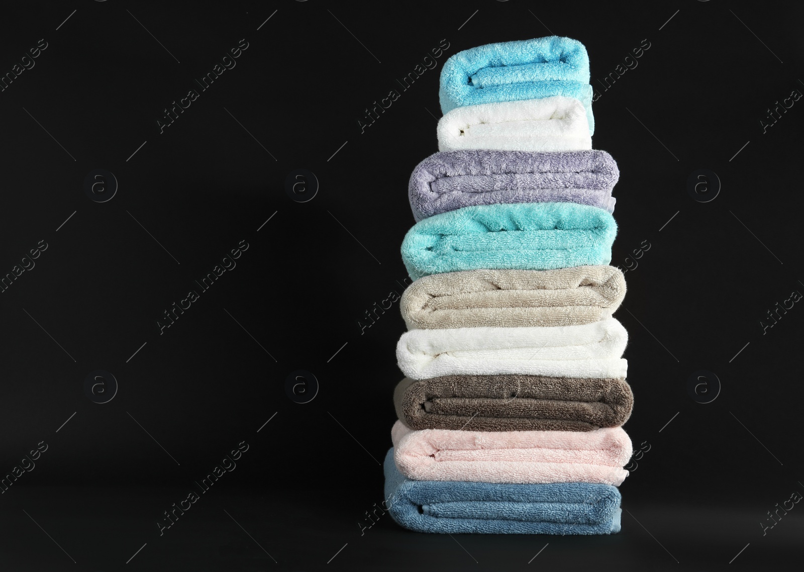 Photo of Different fresh soft terry towels on dark background. Space for text