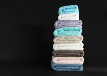 Photo of Different fresh soft terry towels on dark background. Space for text