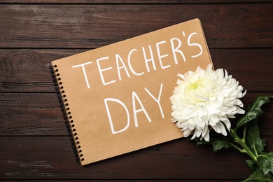 Photo of Notebook with words TEACHER'S DAY and flower on wooden table, flat lay