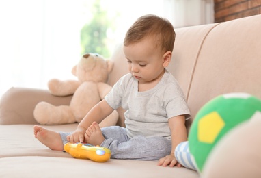 Photo of Adorable little baby with toy phone on sofa at home