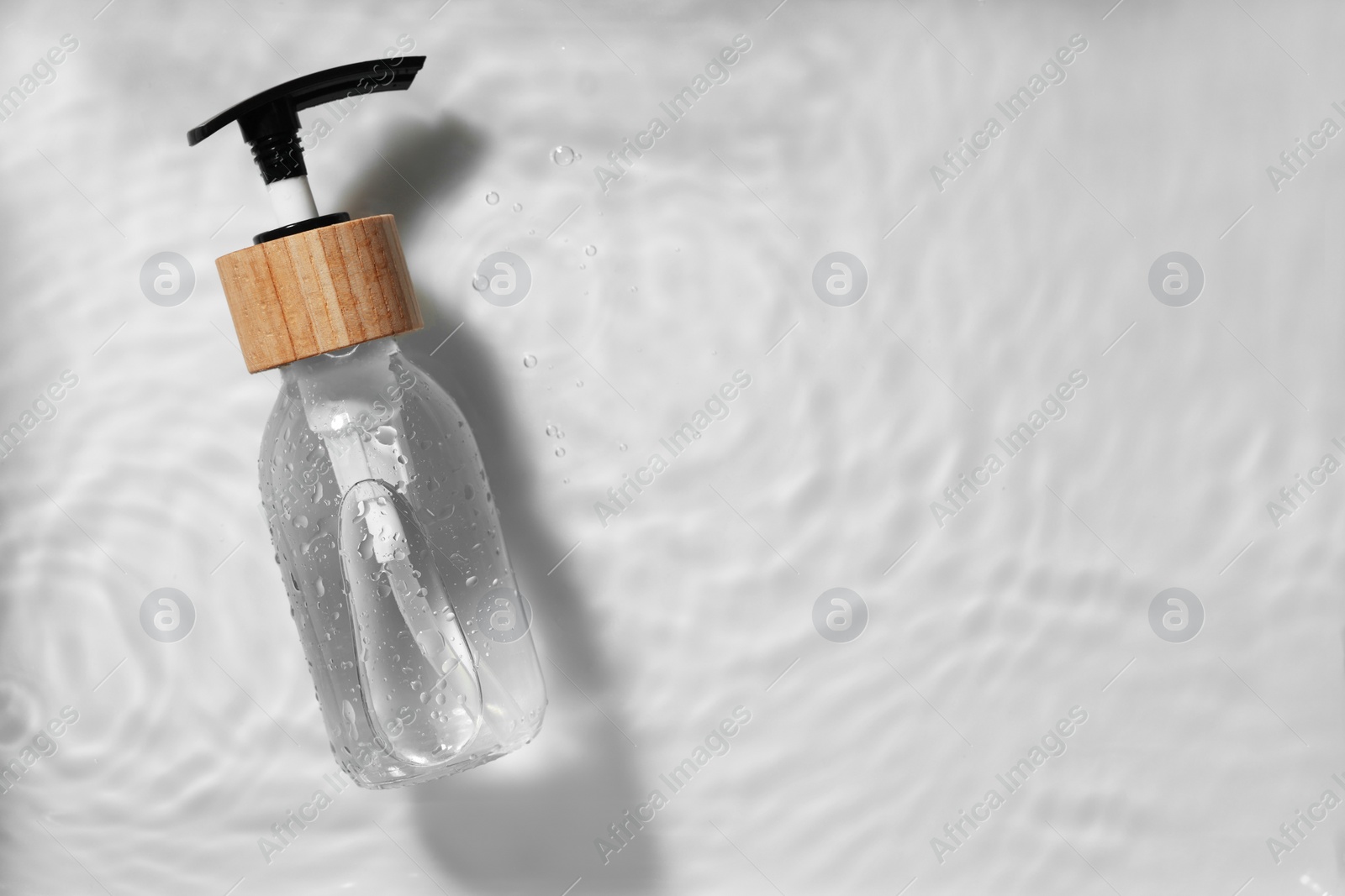 Photo of Bottle of cosmetic product in water on white background, top view. Space for text